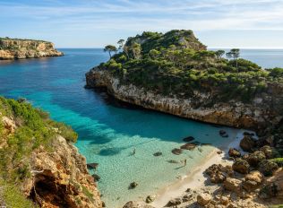 a beach with clear blue water next to cliff