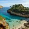 a beach with clear blue water next to cliff